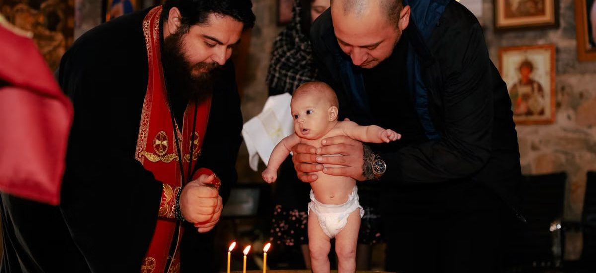 A priest and father performing an Orthodox baptism ceremony with a baby.